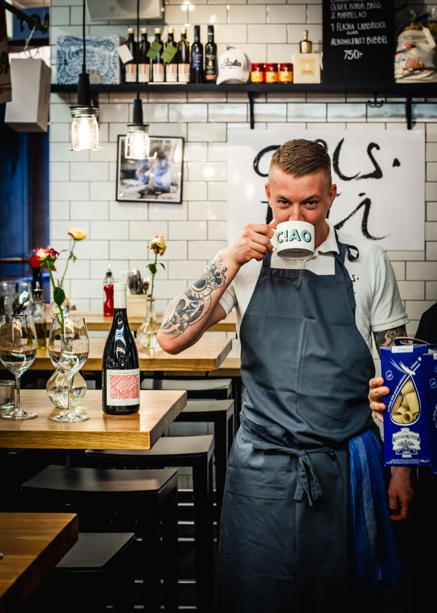 En medarbetare på Carls Deli med en kaffekopp bakom disken